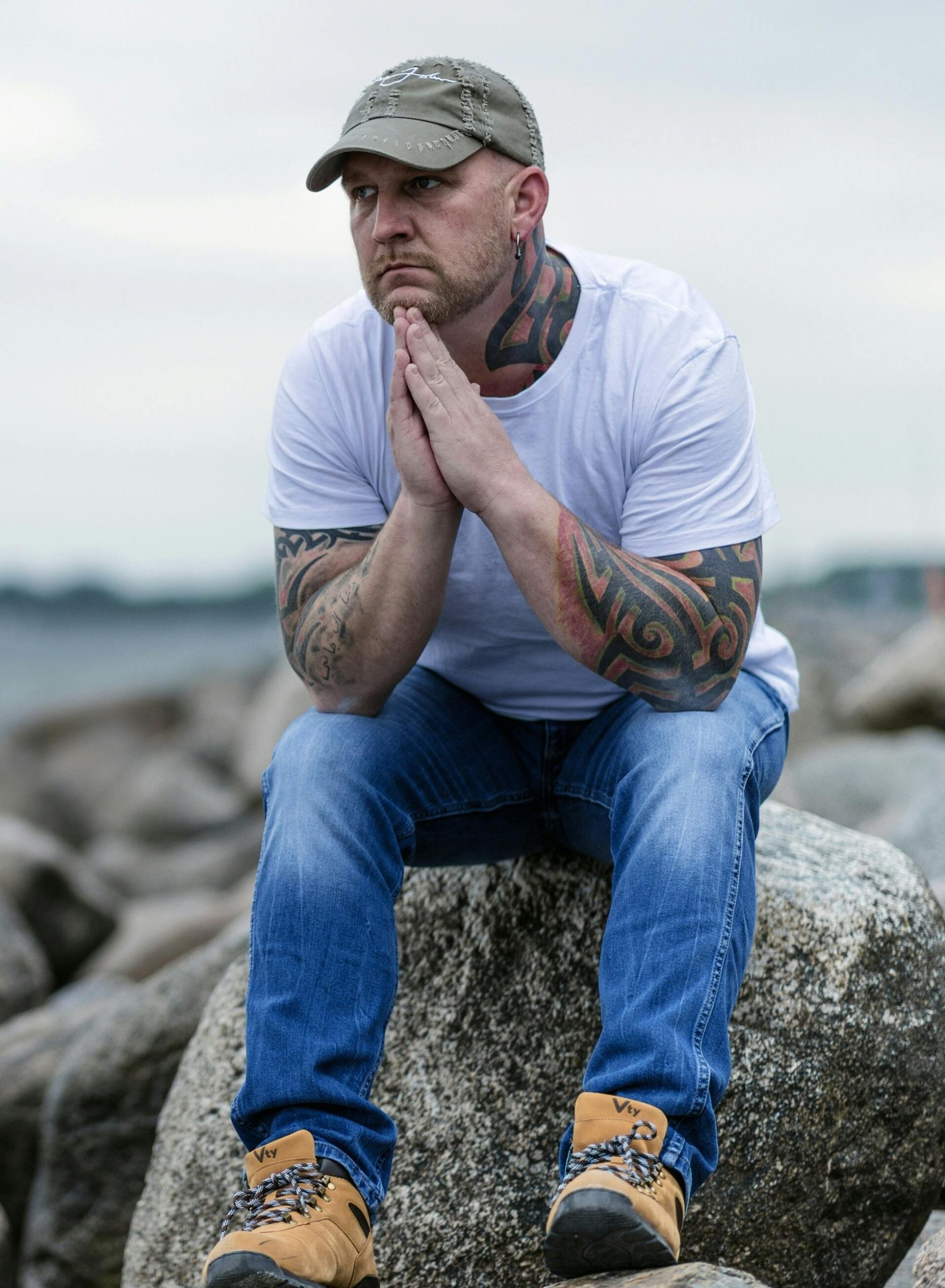A man sitting on rocks near the shore, hands clasped in reflection, symbolizing mindfulness and calm.